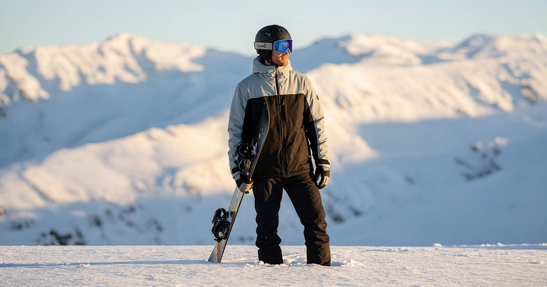 hombre con tabla de snowboard vestido con chaqueta de nieve Chillan by Kano en el medio de la montaña.